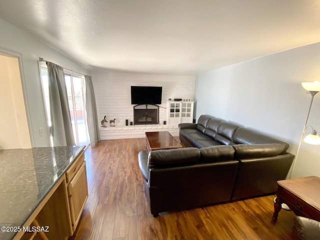 living room with a brick fireplace and dark wood-type flooring