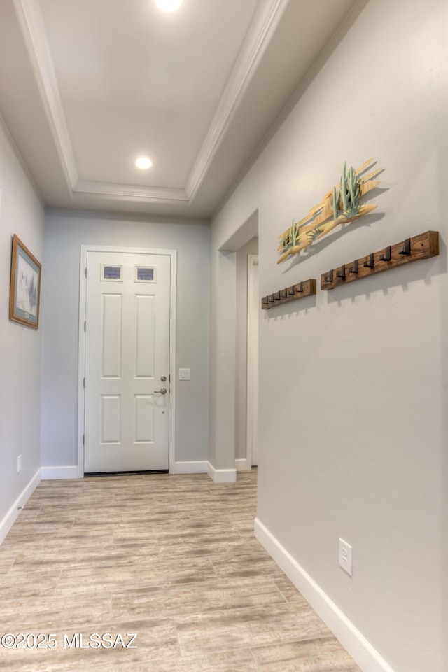 entryway with ornamental molding, light hardwood / wood-style floors, and a raised ceiling