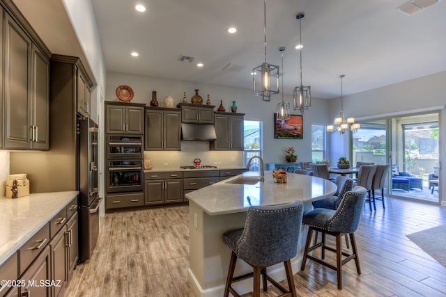 kitchen featuring high quality fridge, an island with sink, sink, hanging light fixtures, and black double oven