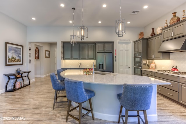 kitchen featuring pendant lighting, light hardwood / wood-style flooring, a breakfast bar area, stainless steel appliances, and a large island with sink