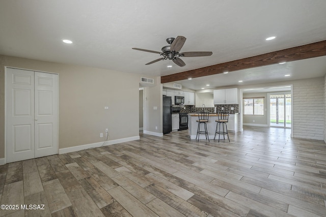 unfurnished living room featuring light wood-style floors, beamed ceiling, baseboards, and a ceiling fan