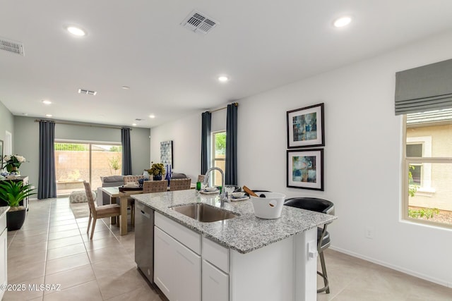 kitchen with dishwasher, white cabinetry, sink, light stone countertops, and a center island with sink