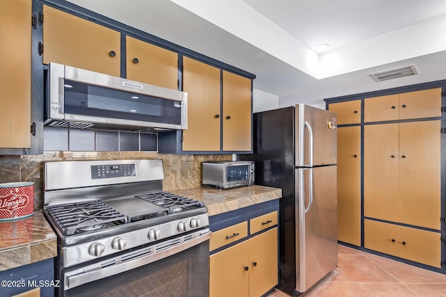 kitchen with stainless steel appliances, a raised ceiling, light tile patterned floors, and backsplash