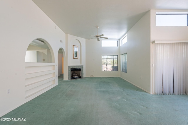 unfurnished living room with a towering ceiling, a tiled fireplace, carpet, ceiling fan, and built in shelves