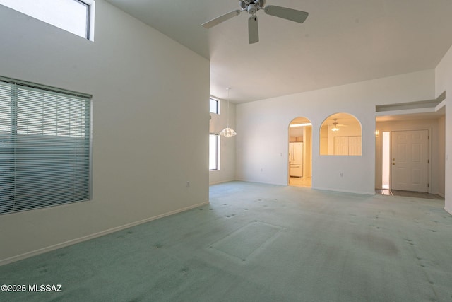 unfurnished living room featuring light colored carpet, ceiling fan, and a high ceiling