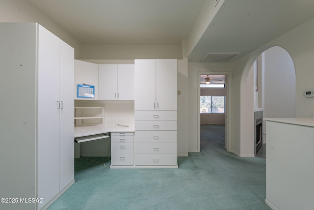 unfurnished office with built in desk, light colored carpet, and ceiling fan