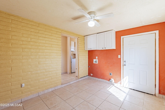 tiled empty room with washer / clothes dryer, a textured ceiling, ceiling fan, and brick wall