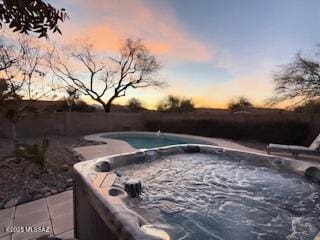 pool at dusk with a fenced in pool and a hot tub