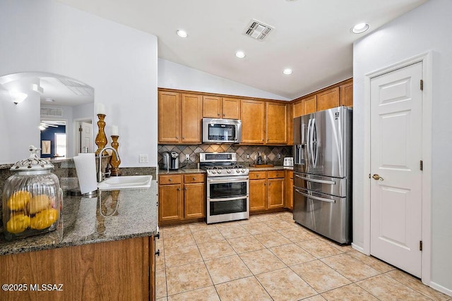 kitchen featuring a sink, brown cabinetry, visible vents, appliances with stainless steel finishes, and lofted ceiling