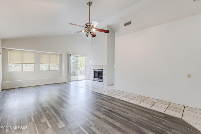 unfurnished living room with a tiled fireplace, high vaulted ceiling, light hardwood / wood-style floors, and ceiling fan