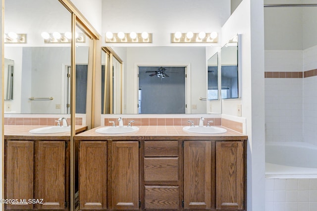 bathroom with tiled tub, vanity, and ceiling fan