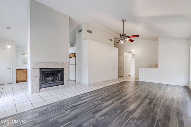 unfurnished living room with a tiled fireplace, ceiling fan, high vaulted ceiling, and light hardwood / wood-style flooring