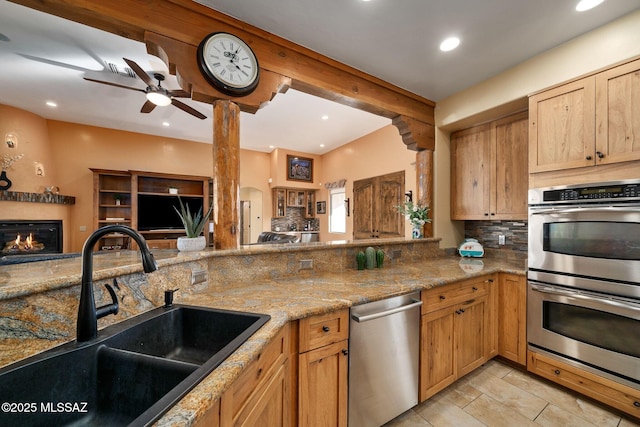 kitchen with tasteful backsplash, sink, light stone counters, kitchen peninsula, and stainless steel appliances