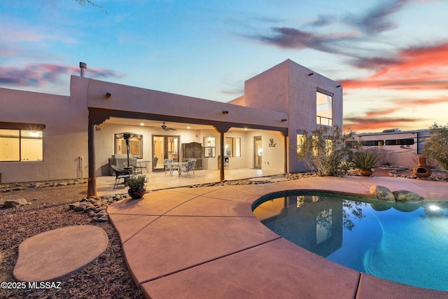 pool at dusk with ceiling fan and a patio area