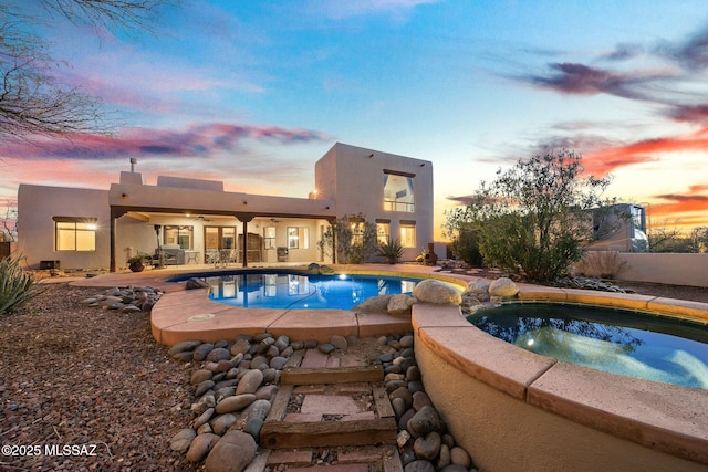 pool at dusk with an in ground hot tub, ceiling fan, and a patio area