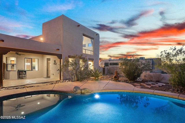 pool at dusk with a patio area and ceiling fan