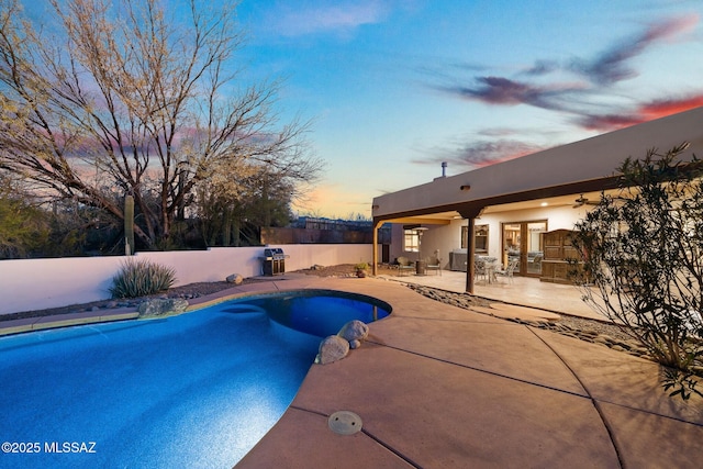 pool at dusk with ceiling fan and a patio