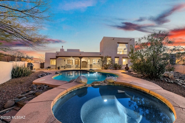 pool at dusk featuring a patio area and an in ground hot tub