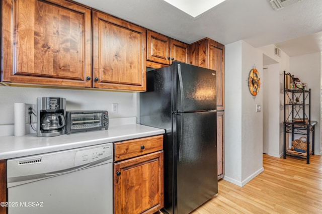 kitchen featuring black fridge, white dishwasher, and light hardwood / wood-style floors