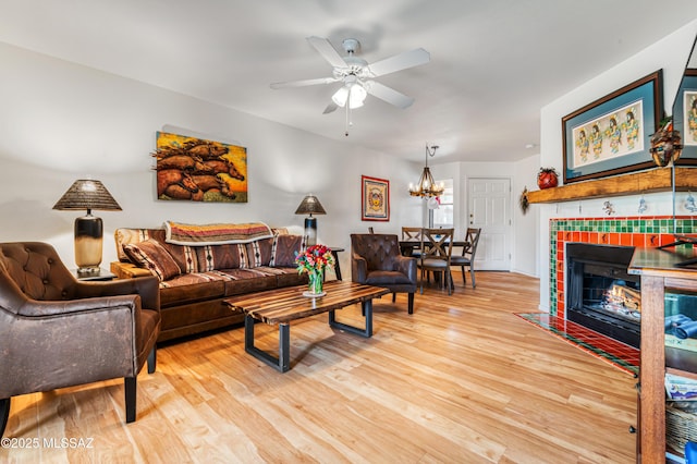 living room featuring a tiled fireplace, ceiling fan with notable chandelier, and light hardwood / wood-style flooring