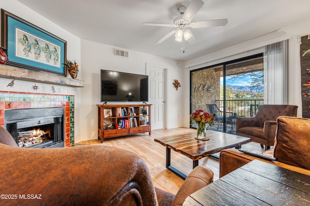 living room with ceiling fan, light hardwood / wood-style floors, and a tile fireplace