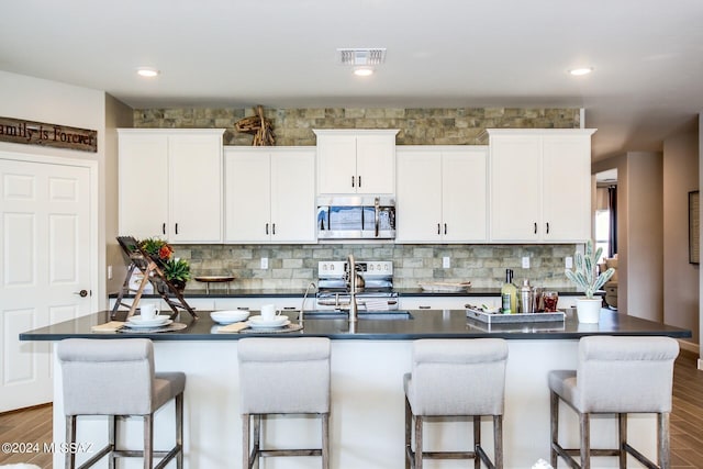 kitchen featuring appliances with stainless steel finishes, a kitchen island with sink, a breakfast bar area, and white cabinets