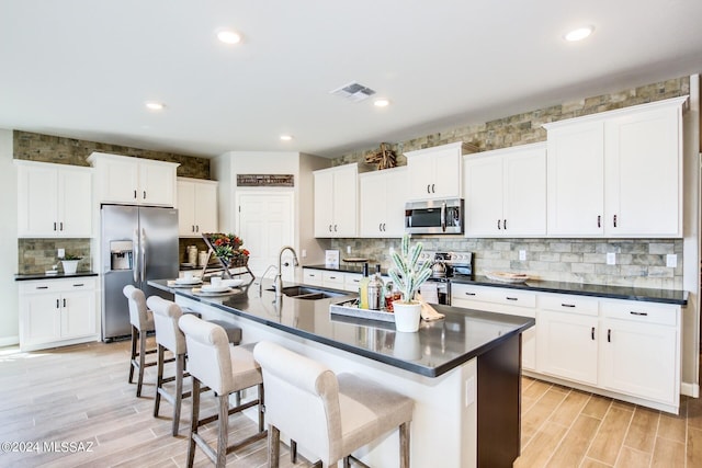 kitchen with a breakfast bar, sink, a center island with sink, appliances with stainless steel finishes, and white cabinets