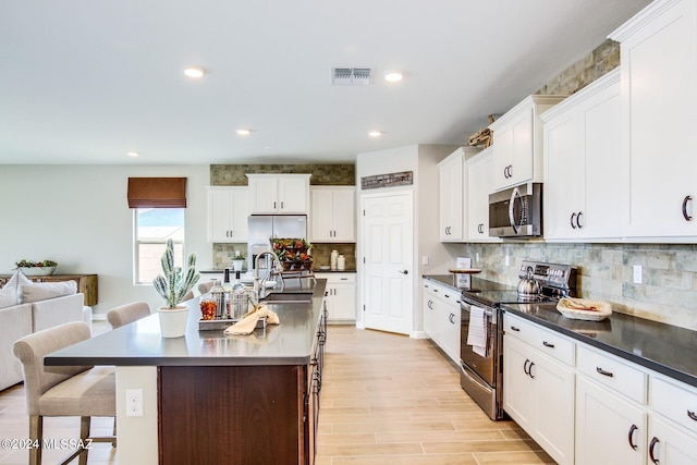 kitchen featuring sink, a kitchen island with sink, white cabinetry, stainless steel appliances, and a kitchen breakfast bar