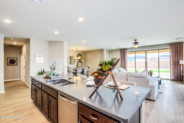 kitchen with sink, stainless steel dishwasher, dark brown cabinetry, a mountain view, and a center island with sink