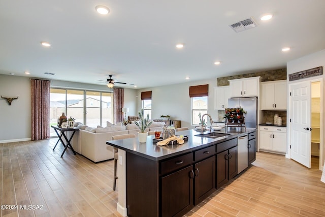 kitchen with stainless steel appliances, white cabinetry, sink, and an island with sink