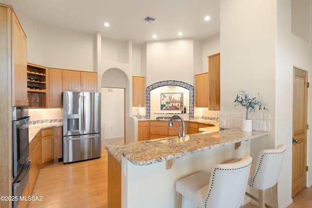 kitchen featuring light stone counters, appliances with stainless steel finishes, a kitchen bar, and kitchen peninsula