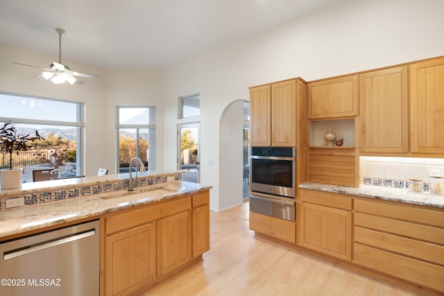 kitchen with sink, ceiling fan, stainless steel appliances, decorative backsplash, and light wood-type flooring