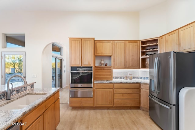 kitchen with sink, decorative backsplash, light stone counters, light hardwood / wood-style floors, and stainless steel appliances