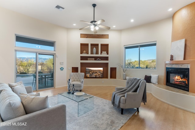 living room with ceiling fan, built in shelves, light hardwood / wood-style flooring, and a healthy amount of sunlight