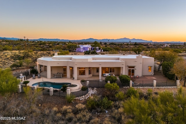 back house at dusk featuring a fenced in pool, a mountain view, and a patio