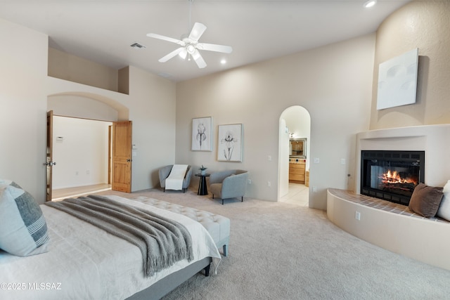 bedroom featuring a high ceiling, ensuite bathroom, light carpet, and ceiling fan