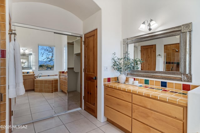 bathroom featuring lofted ceiling, tile patterned flooring, vanity, tasteful backsplash, and tiled bath