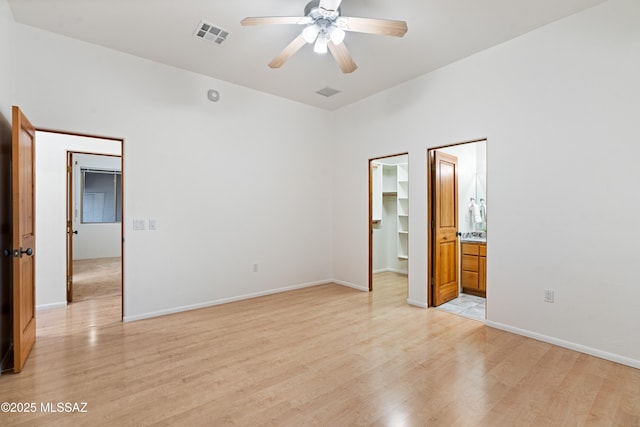 unfurnished bedroom featuring ceiling fan, ensuite bathroom, a walk in closet, a closet, and light wood-type flooring