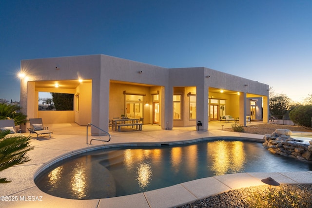 pool at dusk with an in ground hot tub and a patio area