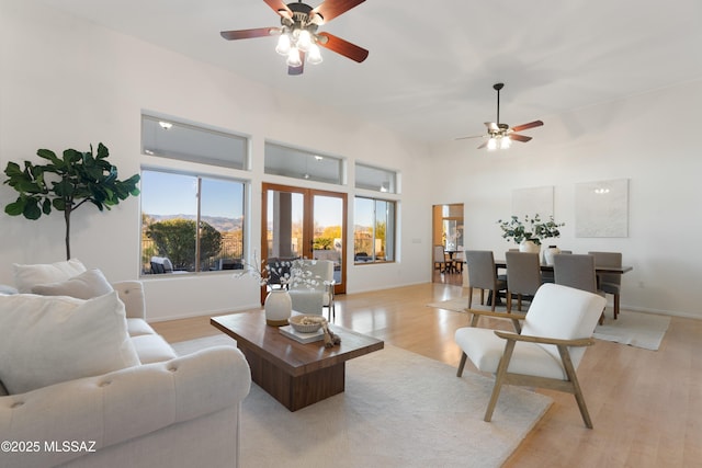 living room with ceiling fan, a towering ceiling, light wood-type flooring, and french doors