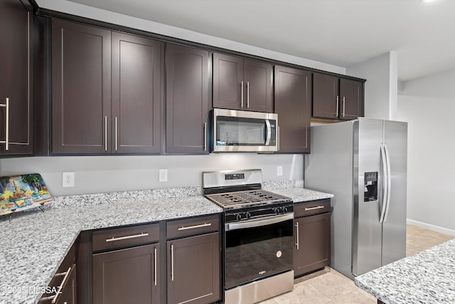 kitchen with stainless steel appliances, dark brown cabinetry, and light stone counters