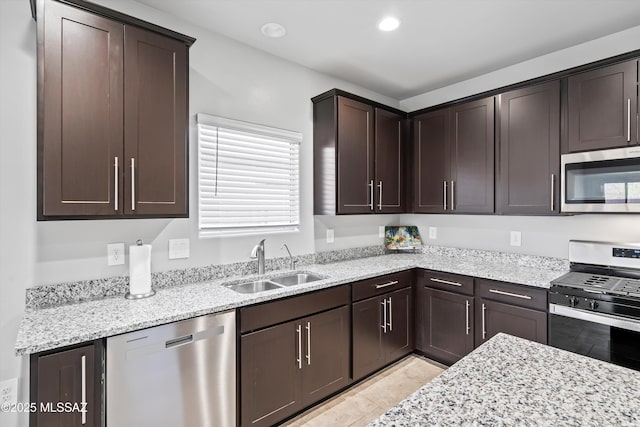 kitchen with dark brown cabinetry, recessed lighting, light stone countertops, stainless steel appliances, and a sink