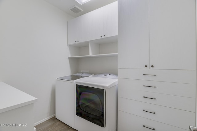 laundry area with light hardwood / wood-style floors, cabinets, and washing machine and clothes dryer