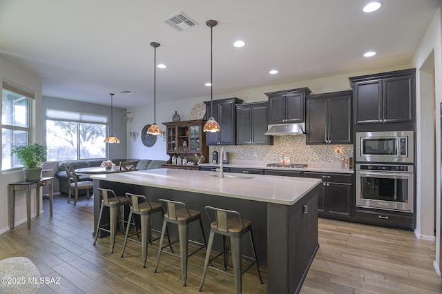 kitchen with decorative light fixtures, a breakfast bar, an island with sink, and appliances with stainless steel finishes