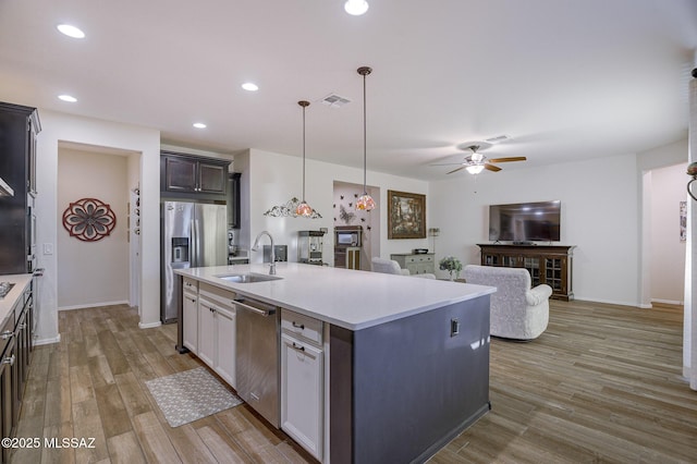 kitchen with appliances with stainless steel finishes, sink, hanging light fixtures, a center island with sink, and light hardwood / wood-style flooring