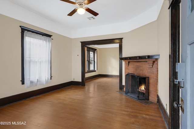 unfurnished living room featuring wood-type flooring, a wealth of natural light, ceiling fan, and a fireplace