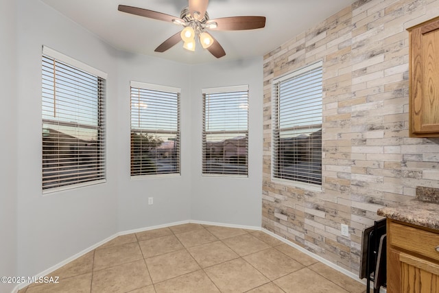 tiled spare room with ceiling fan and brick wall