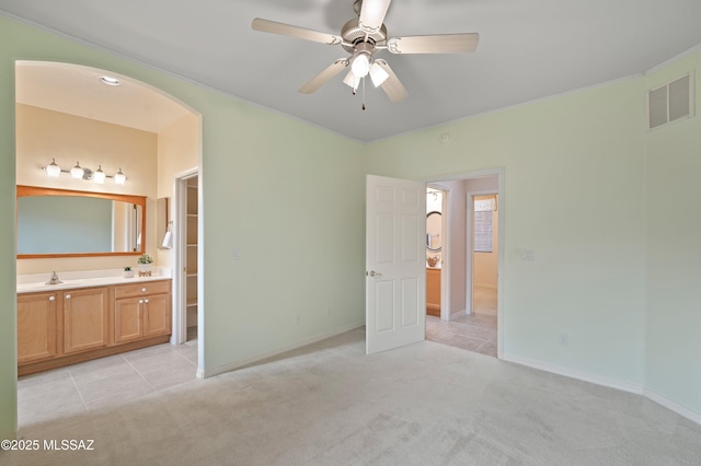 unfurnished bedroom featuring arched walkways, light carpet, a sink, visible vents, and ensuite bath