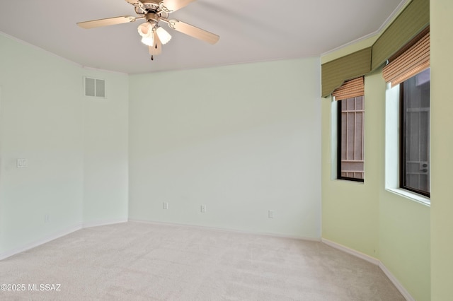 empty room with light carpet, a ceiling fan, visible vents, baseboards, and ornamental molding