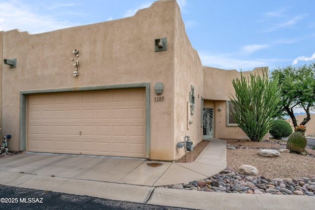 pueblo-style house with driveway, an attached garage, and stucco siding